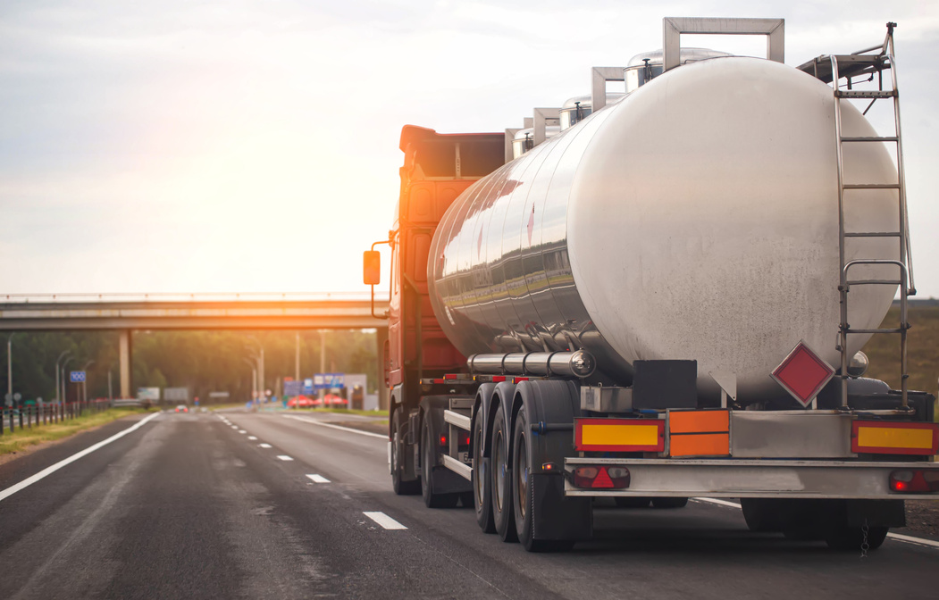 A Truck with a Tank Trailer Transports a Liquid Dangerous Cargo on a Highway against the Backdrop of a Sunset. Copy Space for Text